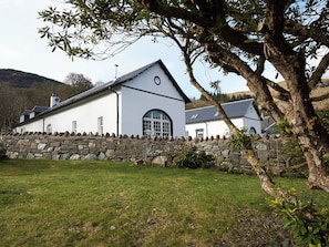 A white building with a stone wall, a large arched window, and a stone chimney. - Glendaruel Lodge - SXXN (Glendaruel)