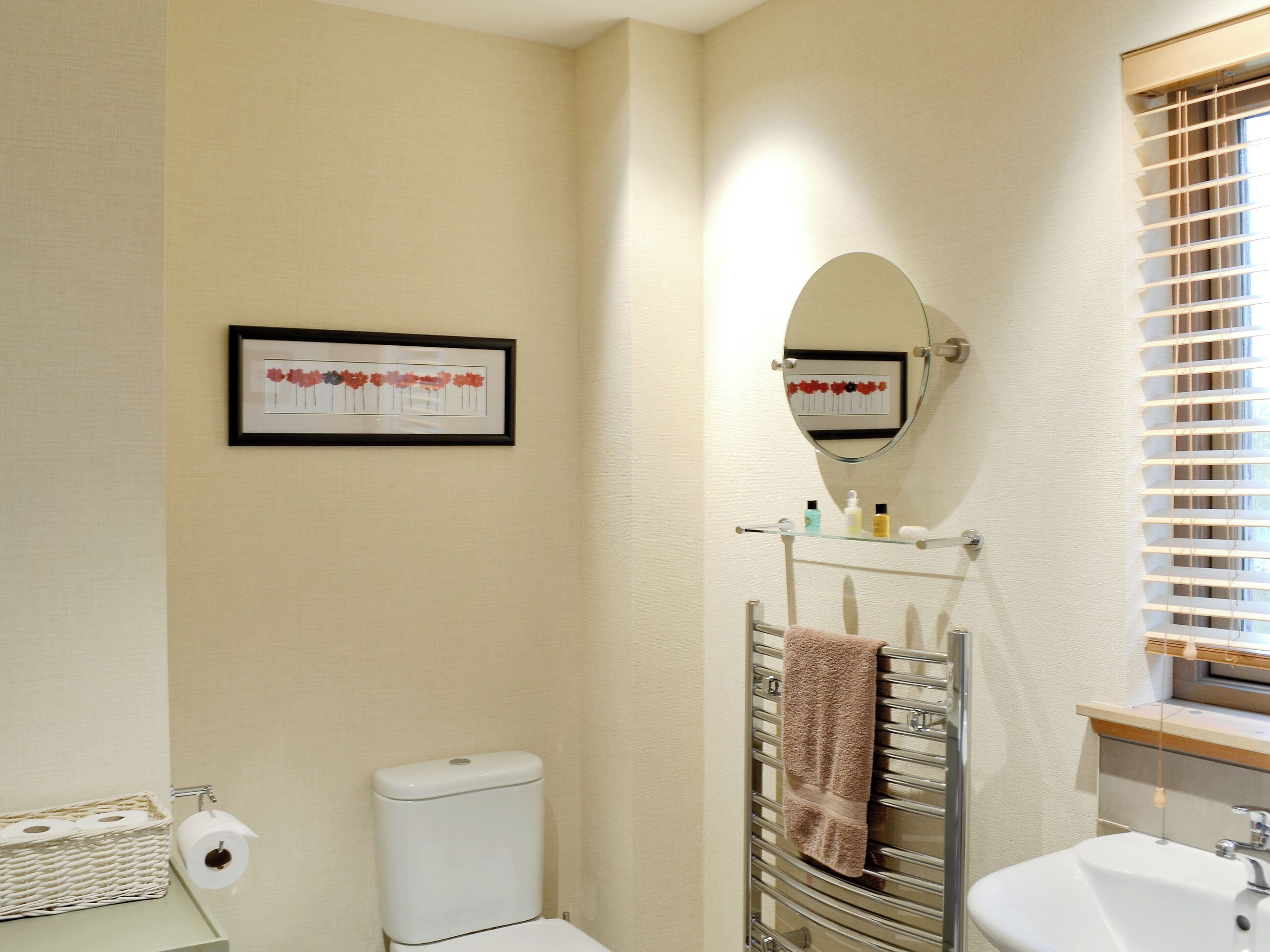 A bathroom with a toilet, a sink, a towel rack, a framed artwork, and a mirror.