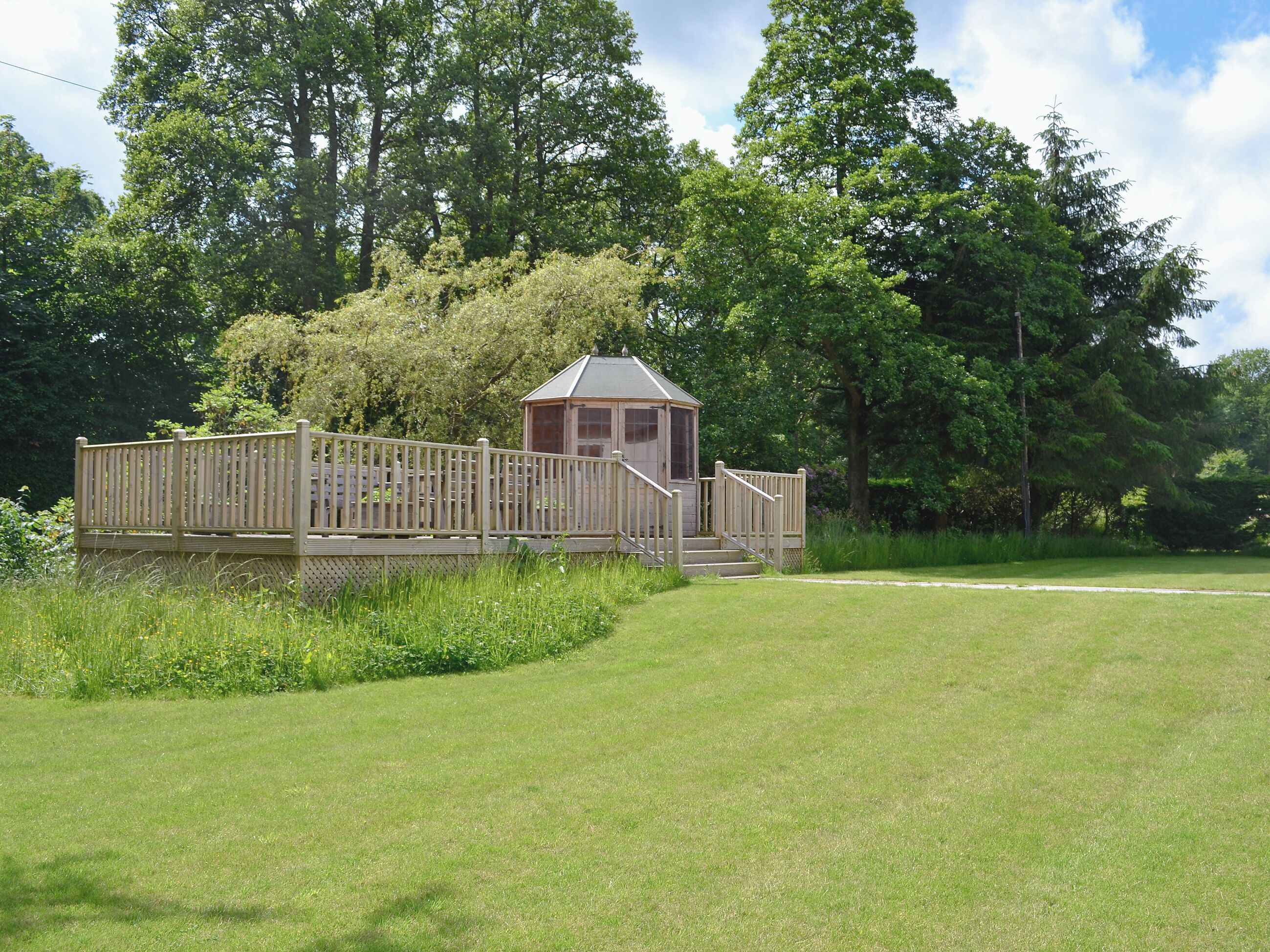 A small wooden structure with a porch and steps, surrounded by lush greenery and trees.