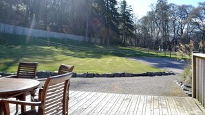 Eine Holzterrasse mit Sitzgelegenheiten im Freien, ein Kiesweg und ein von Bäumen gesäumter, eingezäunter Garten.