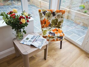 A room with a wooden chair, a table with a newspaper, and a vase with flowers.