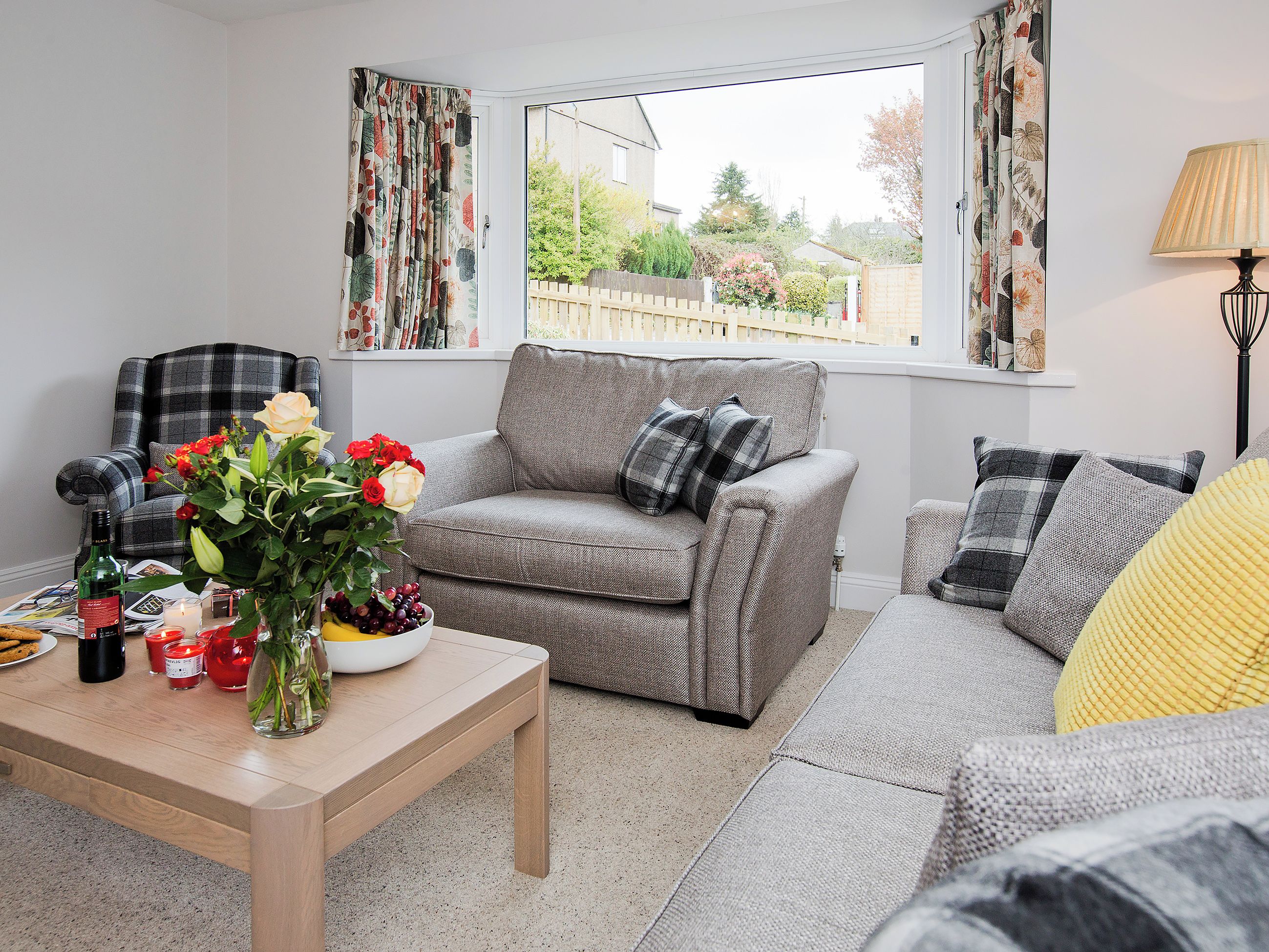 A living room with a grey sofa, a wooden coffee table, and a window with curtains.