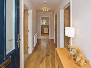 A hallway with wooden flooring, white walls, and a lamp on a table.