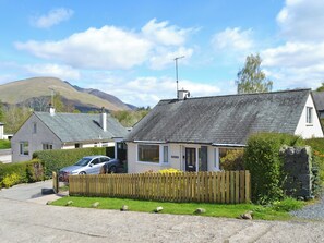 A two-story house with a grey tiled roof, a wooden fence, and a car parked in the driveway.