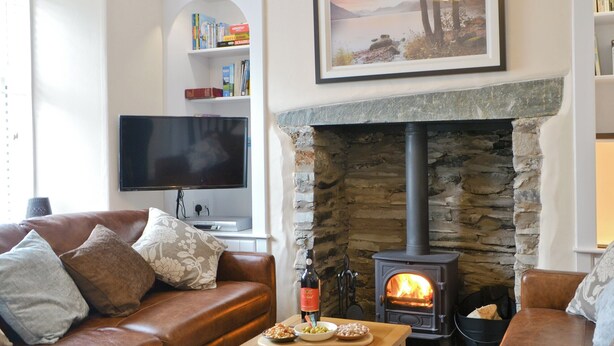 A cozy living room with a stone fireplace, a television, and a bookshelf. - 3 bedroom accommodation in Ambleside (Ambleside)