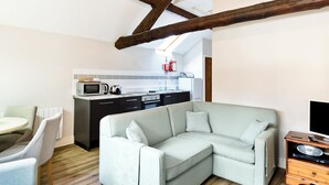 A modern living room with a sectional sofa, a dining area with a round table and chairs, and a kitchen with basic appliances. - Bonsall Cottage - RDDD (Carsington, near Ashbourne)