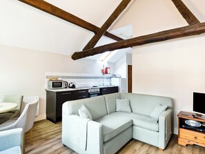 A modern living room with a sectional sofa, a dining area with a round table and chairs, and a kitchen with basic appliances. - Bonsall Cottage - RDDD (Carsington, near Ashbourne)