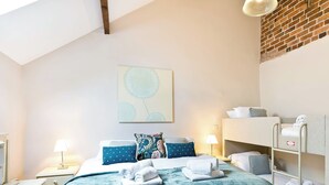 A bedroom with a bunk bed, a bedside table, a lamp, a wall art piece, and a window with a view of a brick wall. - Bonsall Cottage - RDDD (Carsington, near Ashbourne)
