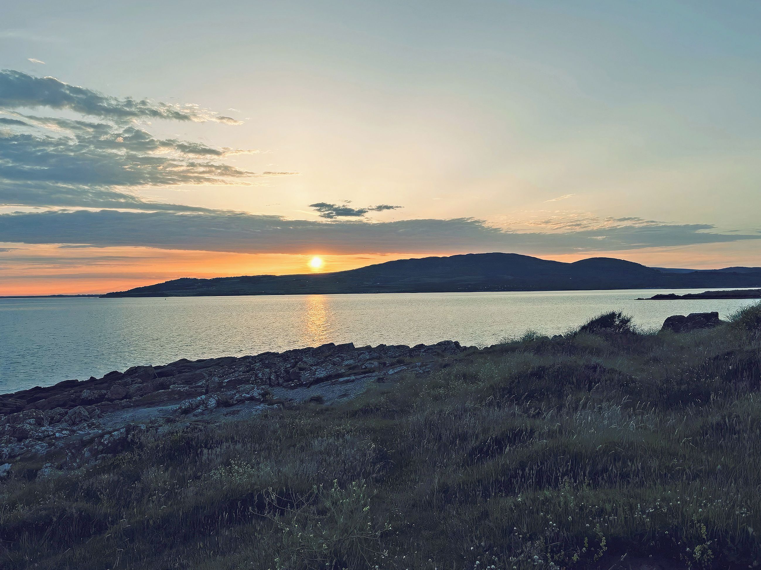 A coastal landscape with a body of water, a distant mountain range, and a rocky shoreline.