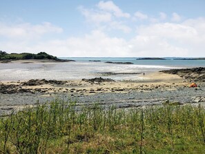 Ein Strand mit felsigem Gelände, einem Zelt und einer Person, die spazieren geht.