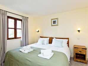 Ett hotellrum med en säng, två sänglampor, ett nattduksbord, en inramad tavla på väggen och ett fönster med gardiner.