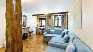 A living room with a wooden floor, a blue sofa, a dining table with chairs, and a stone fireplace. - 2 bedroom accommodation in Carsington, near Ashbourne (Carsington, near Ashbourne)