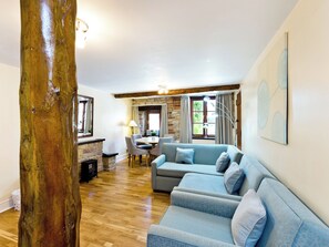 Una sala de estar con piso de madera, un sofá azul, una mesa de comedor con sillas y una chimenea de piedra.