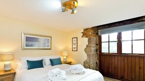 A bedroom with a bed, two bedside tables, a lamp, a framed picture, and a window with a view.