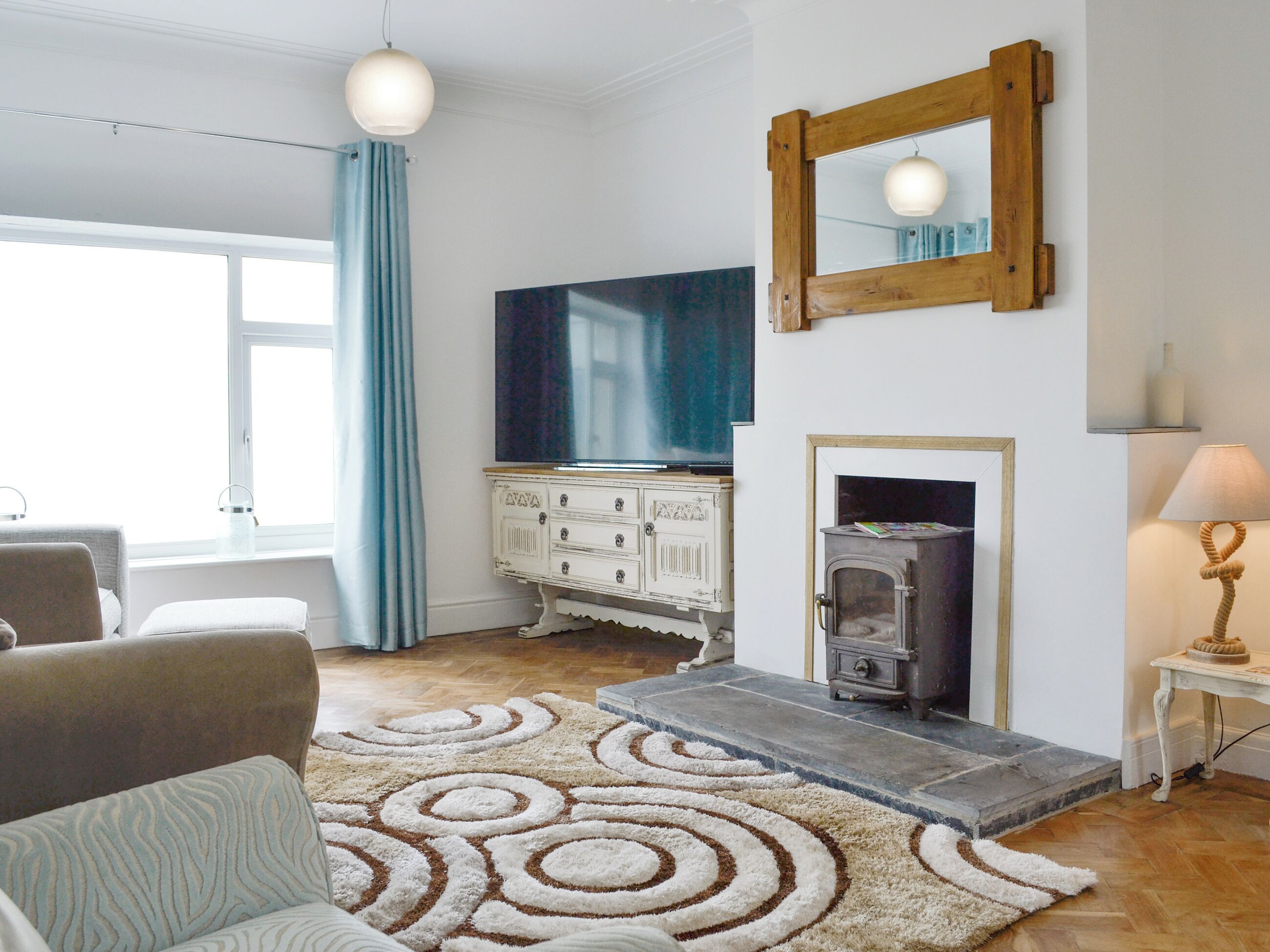 A living room with a fireplace, a television, a white cabinet, and a patterned rug.