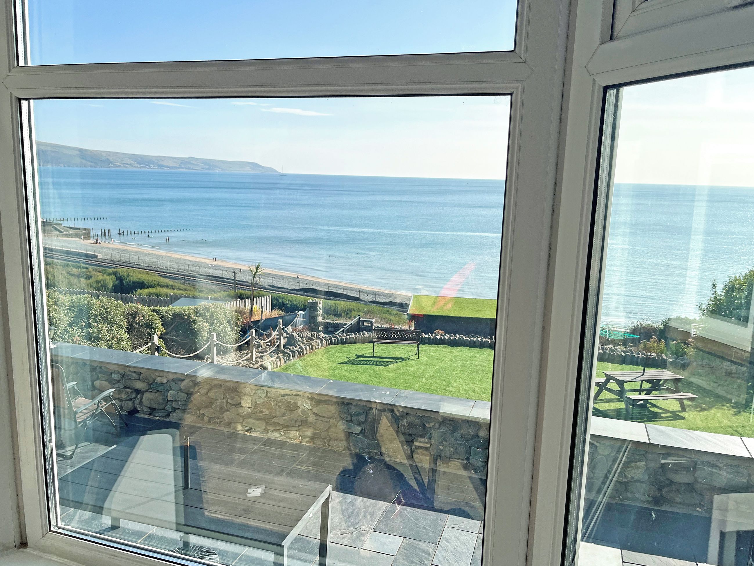 A view of the sea through a window, with a grassy area and a stone wall in the foreground.