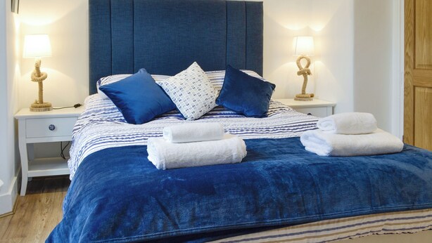 A neatly made bed with blue bedding and pillows, two bedside lamps, and a wooden door in the background. - Brig-Y-Don Bach - UK11309 (Llanaber, near Barmouth)