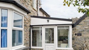 A stone building with a white door and windows, a stone wall, and a sign reading 'Brig-Y-Don Bach.' - Brig-Y-Don Bach - UK11309 (Llanaber, near Barmouth)