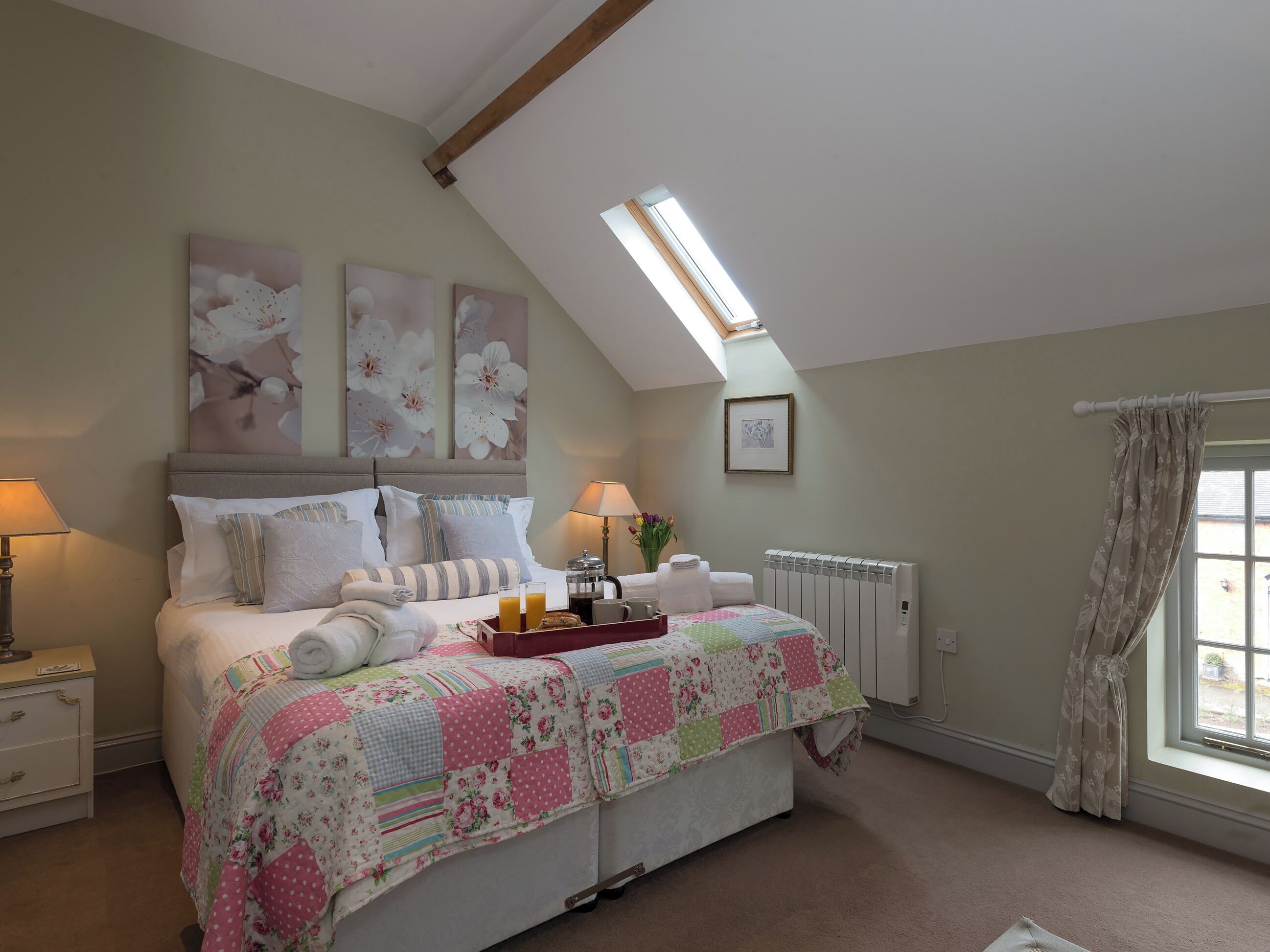Une chambre à coucher comprenant un lit, une table de chevet, un radiateur, une fenêtre avec des rideaux et un puits de lumière.
