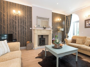 A living room with a fireplace, sofa, television, and a dining table. - No.3 Meynell Mews - UK11366 (Breedon on the Hill)