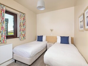 A bedroom with two single beds, a bedside table, a lamp, a window with curtains, and a radiator. - 2 bedroom accommodation in Mungrisdale, near Keswick (Mungrisdale, near Keswick)