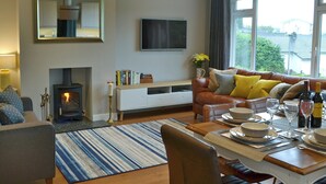 A living room with a fireplace, sofa, dining table set, and a large window with a view. - 3 bedroom accommodation in Ambleside (Ambleside)