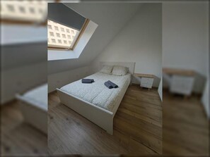 A bedroom with a skylight, a bed with pillows, a nightstand, and a wooden floor. - Charming T2 - Near town center (Dijon)