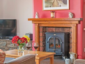 A living room with a fireplace, a television, and a table with flowers and wine glasses. - 2 bedroom accommodation in Mungrisdale, near Keswick (Mungrisdale, near Keswick)