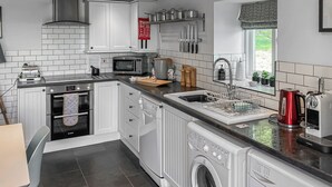 A modern kitchen with white cabinetry, a built-in oven, a microwave, a sink, and a dishwasher. - 1 bedroom accommodation in Garth, near Builth Wells (Garth, near Builth Wells)