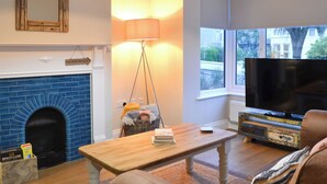 Ein Wohnzimmer mit Kamin, Fernseher, Lampe und Blick ins Freie.