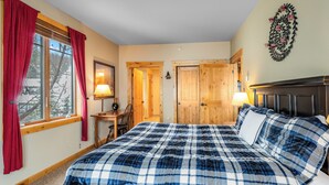 Une chambre à coucher avec un grand lit, des portes en bois, une fenêtre avec des rideaux et un élément de décoration fixé au mur.
