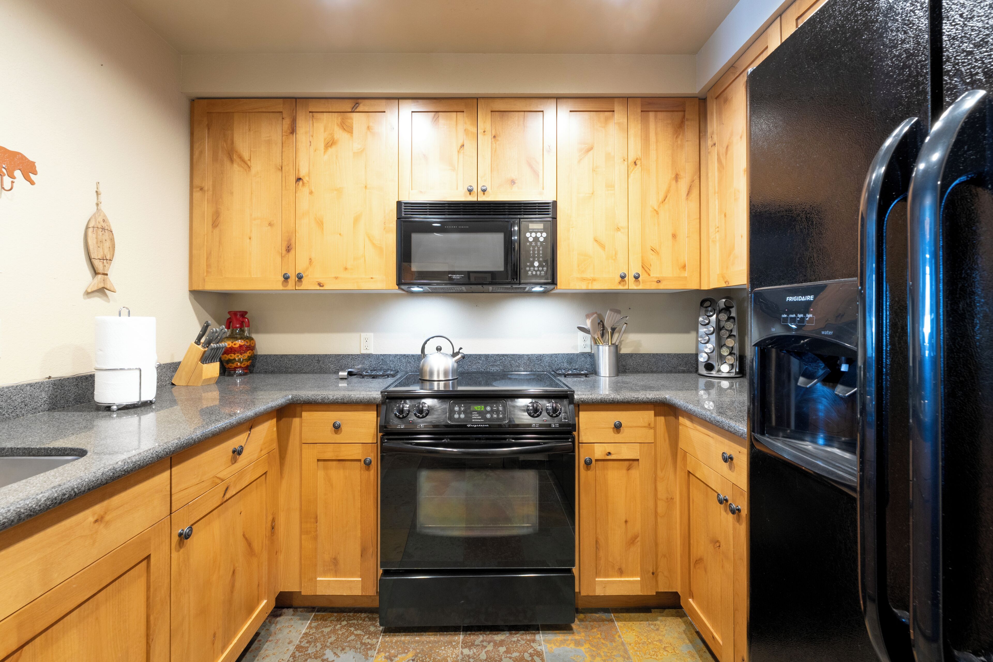 A kitchen with wooden cabinets, a black stove, a microwave, and a refrigerator.