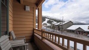 Un balcon en bois, agrémenté de bancs, qui offre une vue sur un village enneigé, avec ses bâtiments et une montagne en arrière-plan.