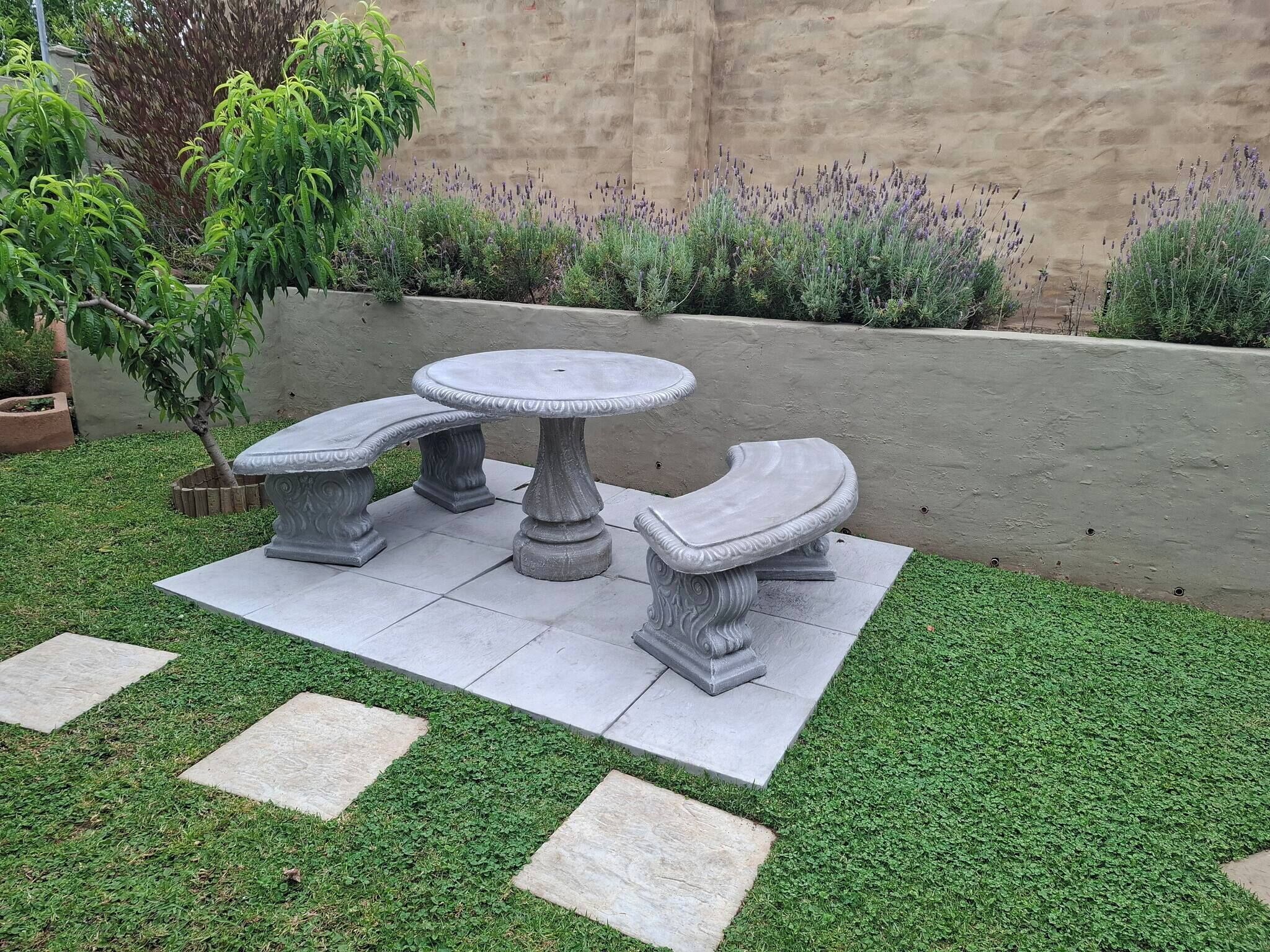 A patio with a stone table and benches, surrounded by a well-maintained lawn and lavender plants.