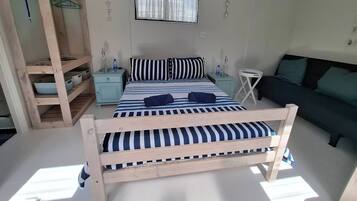 Una habitación con una cama, una mesita de noche, una pequeña mesa, un sofá y una estantería de madera con cestas.