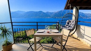 A balcony with a table set for two, a hanging chair, and a view of the sea and mountains. - Zaffiro - Apartment with Lake View Balcony, near Bellagio (Lezzeno)