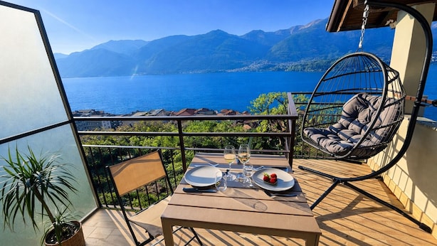 A balcony with a table set for two, a hanging chair, and a view of a lake and mountains. - Zaffiro - Apartment with Lake View Balcony, near Bellagio (Lezzeno)
