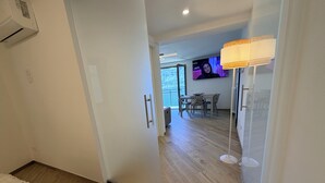 A hotel room with a wooden floor, a bed with a beige blanket, a white door, a dining area with a table and chairs, and a TV mounted on the wall. - Zaffiro - Apartment with Lake View Balcony, near Bellagio (Lezzeno)