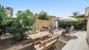 Eine Terrassenanlage im Freien mit Holzmöbeln, einem Grill und einem großen Sonnenschirm.