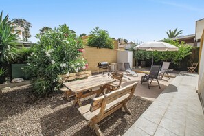 Un patio exterior con mobiliario de madera, una parrilla y un paraguas grande.