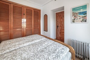 Een slaapkamer met een groot bed, een houten garderobe, een radiator en een spiegel aan de muur.