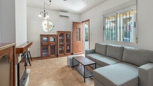 Ein Wohnzimmer mit Sofa, Couchtisch, Schrank, einer Kandelaber und einem Fenster mit Gitterstäben.