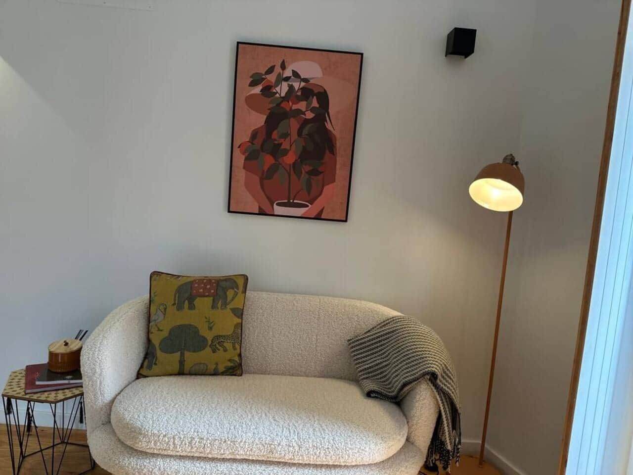 A living room with a sofa, a lamp, a small table, and a framed artwork on the wall.