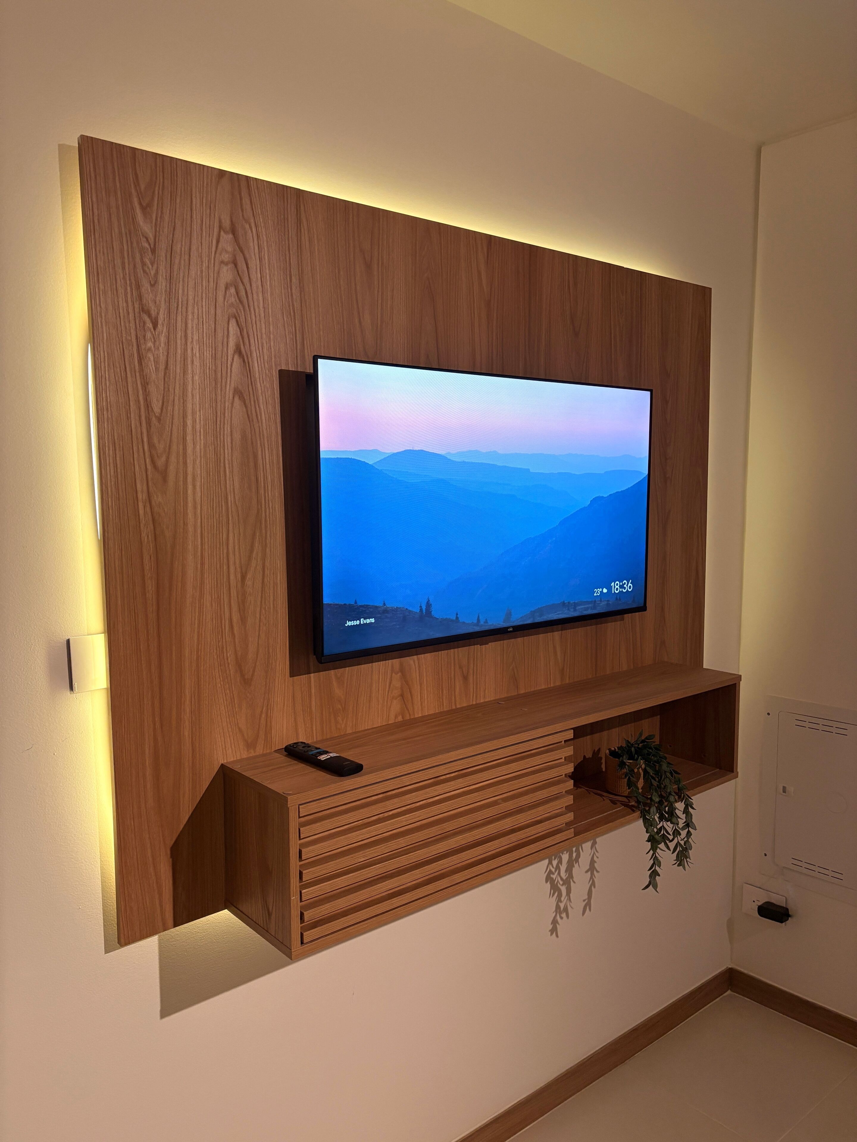Een flatscreen televisie bevestigd aan een houten wand, met een afstandsbediening op een houten plank eronder.