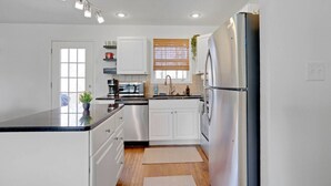 Una cocina moderna con armarios blancos, electrodomésticos de acero inoxidable, horno empotrado y ventana con persianas.