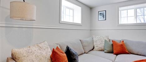A living room with a sectional sofa, two windows, a lamp, and a framed picture on the wall.