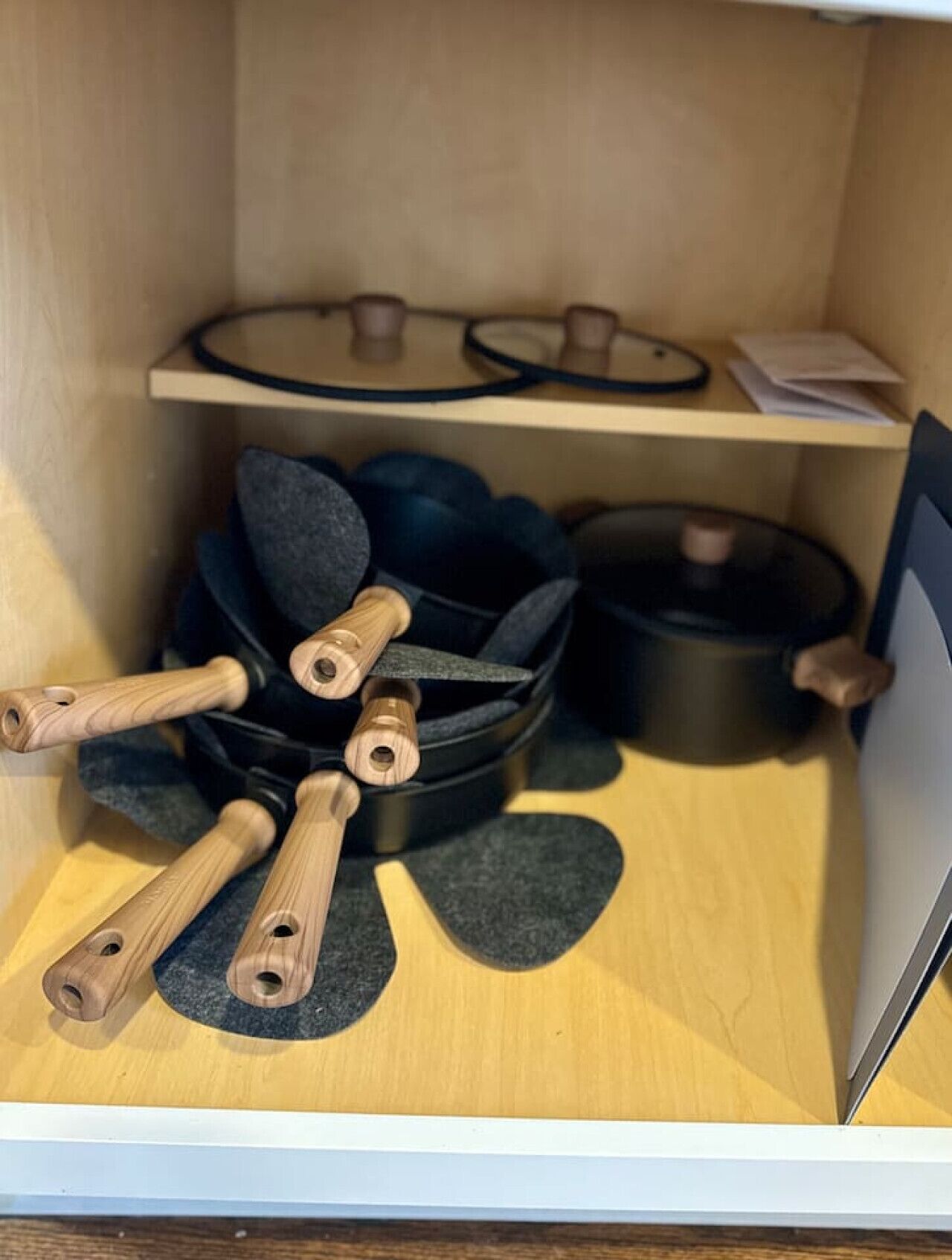 A wooden storage unit with a shelf containing a black bowl, a black pot, and a wooden spoon.