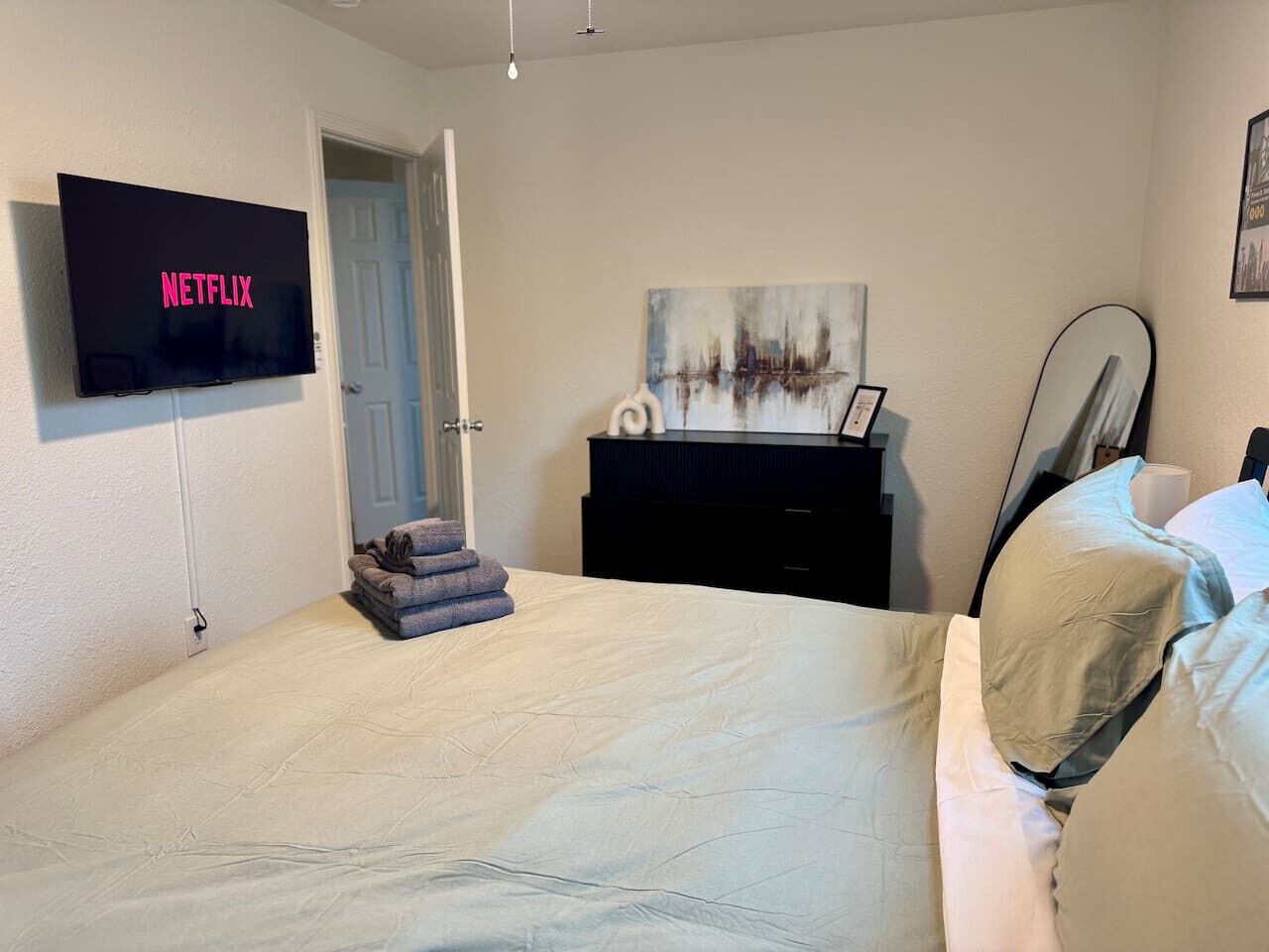 Une chambre à coucher avec un lit, un téléviseur fixé au mur, une commode et une porte.