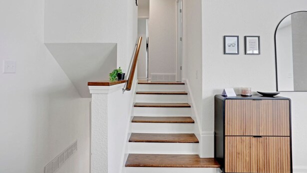 Una escalera de madera con paredes blancas que conduce a una habitación con un armario de madera y un espejo.