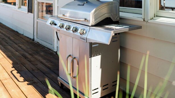 A portable grill unit on a wooden deck, adjacent to a white mobile home with windows. - Island view Crooked Lake cottage, 170' frontage, best views! (Alanson)